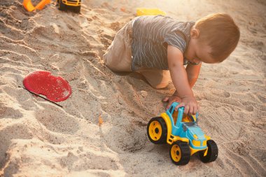 Child playing with toys in sandbox. Little boy having fun on playground in sandpit. Outdoor creative activities for kids. Summer and childhood concept.