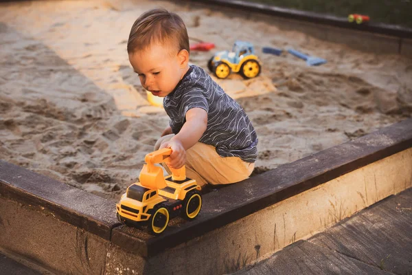 Boy playing with toys in sandbox. Child having fun on playground in sandpit. Outdoor creative activities for kids. Summer and childhood concept.