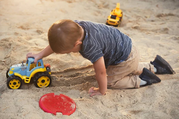 Child playing with toys in sandbox. Little boy having fun on playground in sandpit. Outdoor creative activities for kids. Summer and childhood concept.