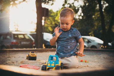 Kid playing with toys in sandbox. Little boy having fun on playground in sandpit. Outdoor creative activities for kids. Summer and childhood concept.