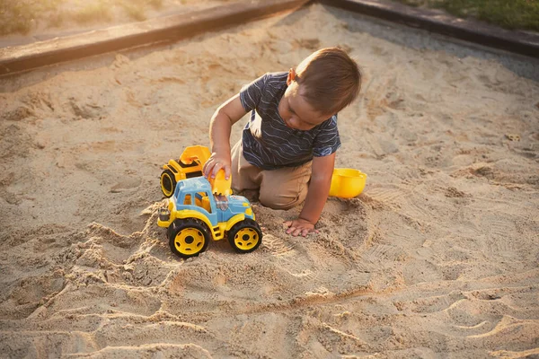 Child playing with toys in sandbox. Little boy having fun on playground in sandpit. Outdoor creative activities for kids. Summer and childhood concept.