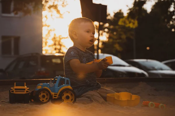 Kid playing with toys in sandbox. Little boy having fun on playground in sandpit. Outdoor creative activities for kids. Summer and childhood concept.