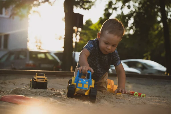 Kid playing with toys in sandbox. Little boy having fun on playground in sandpit. Outdoor creative activities for kids. Summer and childhood concept.
