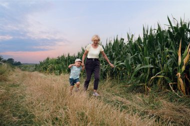 Grandmother and child running outdoor. Happy family on a road near corn field during summer sunset. Generation, happiness vitality concept.