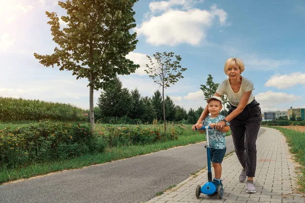 Grandmother Supporting Holding Her Years Old Grandson Ride Scooter Sunny — Zdjęcie stockowe