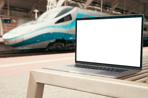 Laptop with white screen in railway station. Empty copy space, blank screen mockup. Soft focus laptop with train background. Travel, study and work outside office concept.