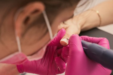 Manicure salon master removes nail polish uses an electric nail file. Woman getting nail manicure. Professional manicure in beauty salon. Hygiene and care for hands. Beauty industry concept.