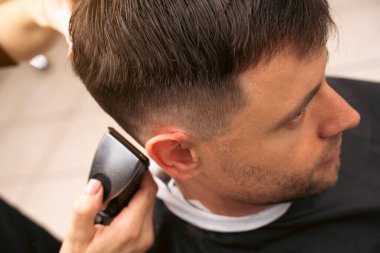 Hair salon master trimmed client hair with electric razor at barber shop. Male client getting haircut by hairdresser. Hair care, beauty industry, barber concept.