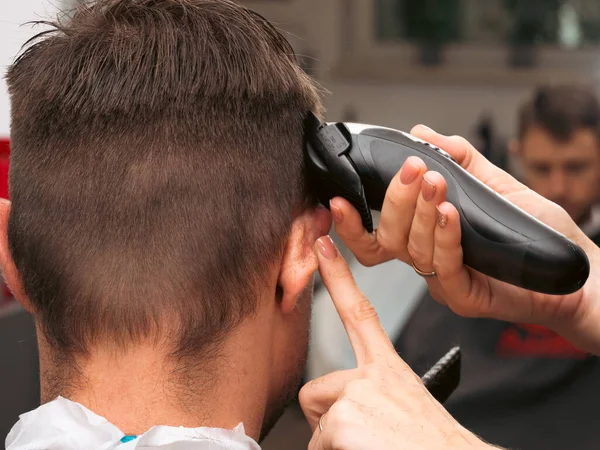 Hair salon master trimmed client hair with electric razor at barber shop. Male client getting haircut by hairdresser. Hair care, beauty industry, barber concept.