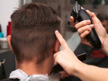 Hair salon master trimmed client hair with electric razor at barber shop. Male client getting haircut by hairdresser. Hair care, beauty industry, barber concept.