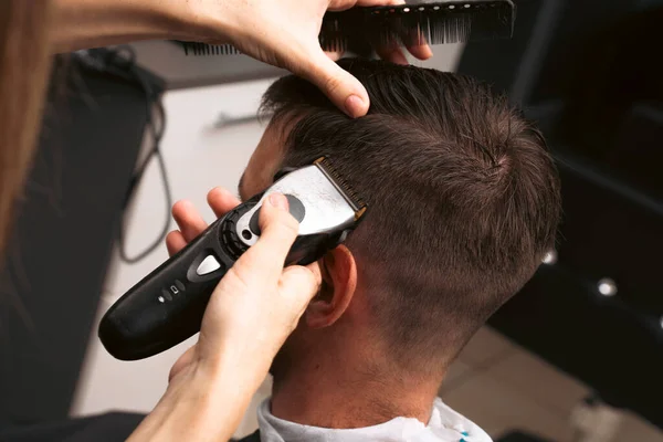 Hair salon master trimmed client hair with electric razor at barber shop. Male client getting haircut by hairdresser. Hair care, beauty industry, barber concept.