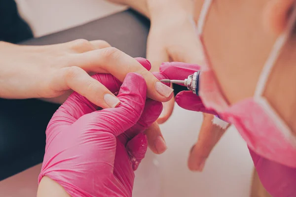 Manicure salon master removes nail polish uses an electric nail file. Woman getting nail manicure. Professional manicure in beauty salon. Hygiene and care for hands. Beauty industry concept.