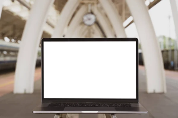 Laptop with white screen in railway station. Empty copy space, blank screen mockup. Soft focus laptop in railway station background. Travel, study and work outside office concept.