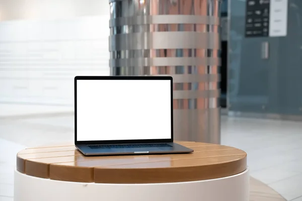 Laptop with white screen in business office or shopping mall. Empty copy space, blank screen mockup. Soft focus laptop with interor background. Travel, study and office work concept.