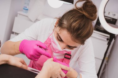 Manicure salon master removes cuticles with nail scissors. Woman getting nail manicure. Professional manicure in beauty salon. Hygiene and care for hands. Beauty industry concept.