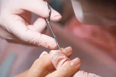Manicure salon master removes cuticles with nail scissors. Woman getting nail manicure. Professional manicure in beauty salon. Hygiene and care for hands. Beauty industry concept.