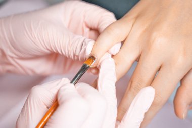 Manikür salonu müdürü tırnağa fırçayla cila çiziyor. Güzellik salonunda profesyonel manikür. Hijyen ve el bakımı. Tırnak sanatı, el bakımı, güzellik endüstrisi konsepti.