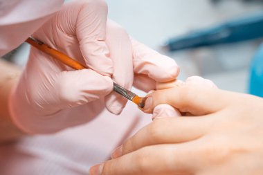 Manikür salonu müdürü tırnağa fırçayla cila çiziyor. Güzellik salonunda profesyonel manikür. Hijyen ve el bakımı. Tırnak sanatı, el bakımı, güzellik endüstrisi konsepti.