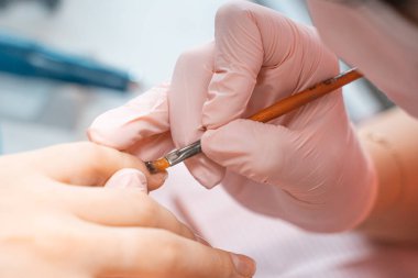 Manikür salonu müdürü tırnağa fırçayla cila çiziyor. Güzellik salonunda profesyonel manikür. Hijyen ve el bakımı. Tırnak sanatı, el bakımı, güzellik endüstrisi konsepti.
