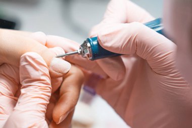 Manicure salon master removes nail polish uses an electric nail file. Woman getting nail manicure. Professional manicure in beauty salon. Hygiene and care for hands. Beauty industry concept.