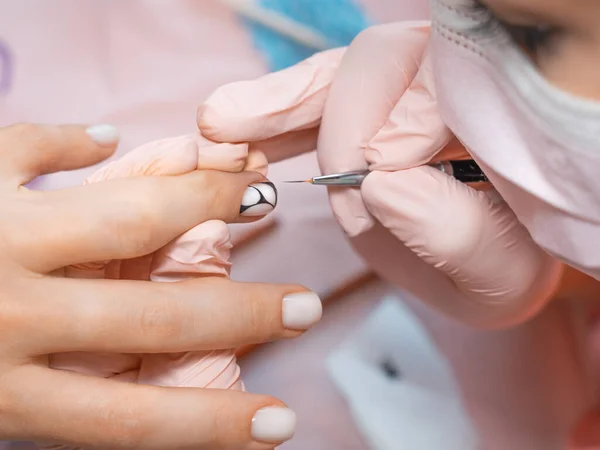 Manicure salon master drawing varnish on the nail tip with a thin brush. Professional manicure in beauty salon. Hygiene and care for hands. Nail art, hands care, beauty industry concept.