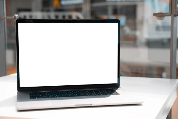 Laptop with white screen in business office or shopping mall. Empty copy space, blank screen mockup. Soft focus laptop with interor background. Travel, study and office work concept.