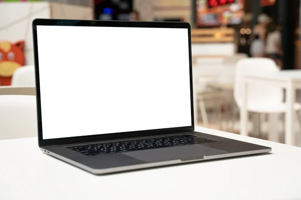 Laptop with white screen in business office or shopping mall. Empty copy space, blank screen mockup. Soft focus laptop with interor background. Travel, study and office work concept.