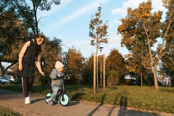 Happy family mother teaches child son to ride a bike in the Park. Crying boy fear, afraid idea. Family, childhood concept. Mother help her son ride a bicycle.