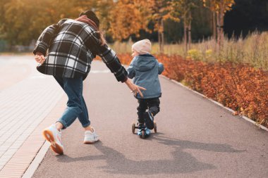 Anne, oğlunun scooter sürmesine yardım et. Mutlu aile annesi çocuğuna parkta scooter sürmeyi öğretiyor. Çocukluk ebeveynliği fikrini destekleyin. Mutlu aile kavramı.