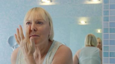 Beyaz kadın yüzüne krem ve losyon sürüyor.