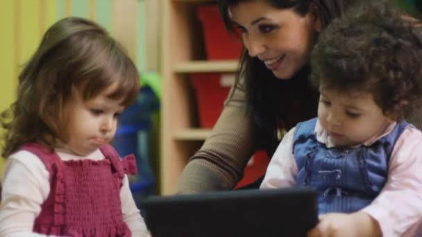 Pädagogin und kleine Mädchen spielen im Kindergarten mit Touchpad-Computer