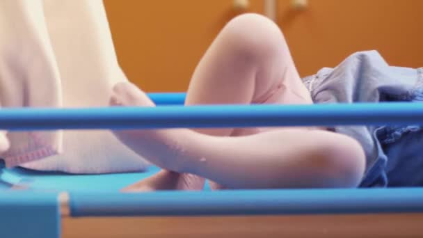 Little child going to sleep in cot at kindergarten with teacher covering her. — Stock Video