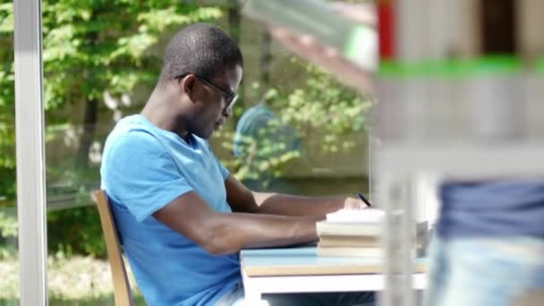 Chico afroamericano y estudiante universitaria caucásica leyendo libro en biblioteca — Vídeo de stock