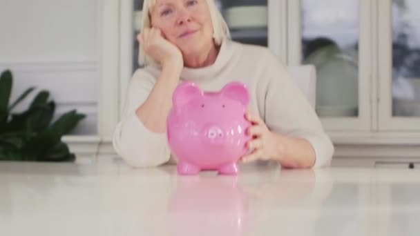 Old woman showing piggybank and euro coin — Stock Video