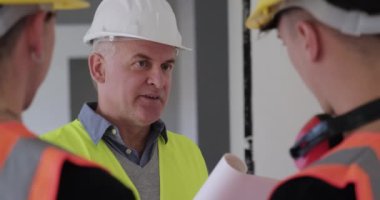 İnşaat alanında çalışanlar. Yeni apartmanda çalışan adamlar. Mühendisle konuşan bir işçiyle ekip çalışması. Kendine güvenen mimarın portresi kameraya bakıyor ve gülümsüyor, yavaş çekim.