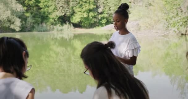 学校の若い女性 公園で大学テストのために話して勉強する4人の女性の友人 幸せな白人とアフリカ系アメリカ人の学生による授業の復習 — ストック動画