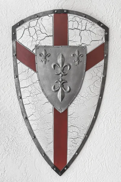 Металлический щит с красным крестом на белой текстурной стене — стоковое фото