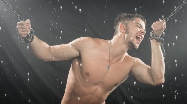 Strong man in chains posing under the rain, aqua studio clipart