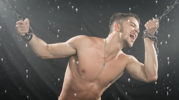 Strong man in chains posing under the rain, aqua studio — Stock Photo, Image