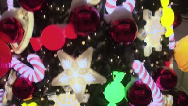 Árvore de Natal decorada na rua nevada durante a queda de neve. Decoração de árvore de Natal com brinquedos, caramelos de cana de doces, bolas e homem de gengibre. Iluminados brinquedos de árvore de ano novo — Vídeo de Stock