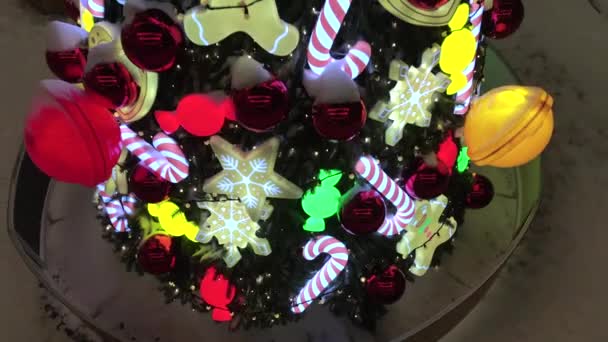 Árbol de Navidad decorado en la calle nevada durante las nevadas. Decoración del árbol de Navidad con juguetes, caramelos de caña de caramelo, bolas y hombre de jengibre. Juguetes de árbol de año nuevo iluminados — Vídeos de Stock