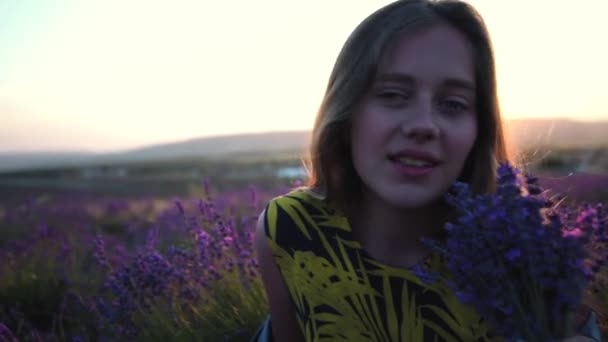 Hermosa joven agricultora huele ramo de flores de lavanda en el campo en la granja de lavanda en la puesta del sol — Vídeo de stock