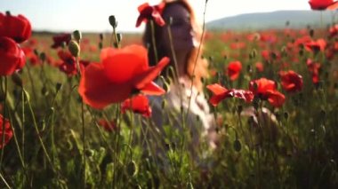 Ön planda gelincik tarlası var. Arka planda da da beyaz gömlekli kızıl saçlı genç bir kız.