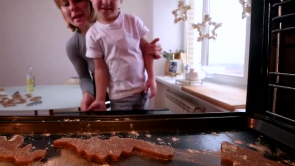 Jong mam met rood kort haar en blond zoon zet zelfgemaakte peperkoek koekjes in de oven — Stockvideo