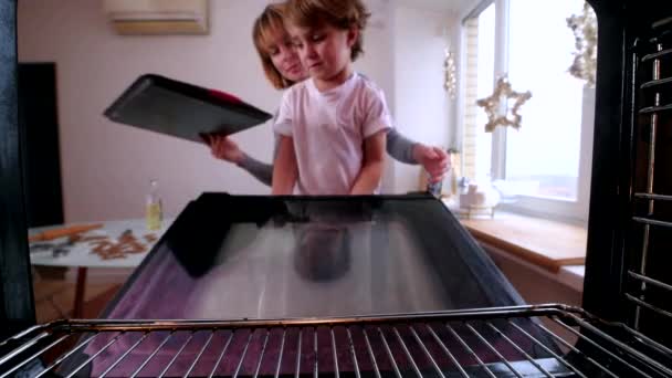 Jong mam met rood kort haar en blond zoon zet zelfgemaakte peperkoek koekjes in de oven — Stockvideo