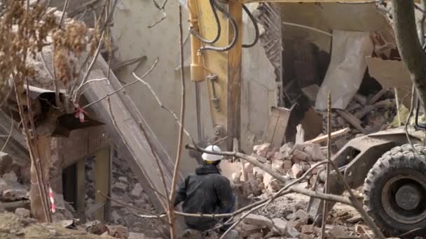 Inženýr s ochrannou helmou se dívá na demolici, ničení staré budovy, bagr bourá vinobraní domu. Dekonstrukce živého objektu. Městská obnova 4k Vysoce kvalitní zpomalené video — Stock video