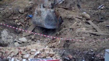 Escavator, kar yağarken donmuş zemini kazıyor. Kışın kır köyünde yaşayan eski bir evin yeniden inşası. Kentsel Yenilenme 4k yüksek kaliteli sinematik video
