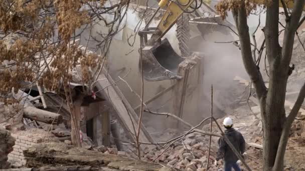 A védősisakos mérnök megnézi a bontást, a régi épület lerombolását, a kotró lerombolja a régi házat. Élő tárgy dekonstrukciója. Városi megújulás 4k Kiváló minőségű lassított felvétel — Stock videók