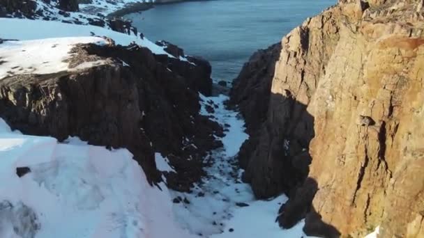 Volo aereo invernale attraverso canyon panoramico sopra le onde che rotolano sulla riva artica dell'oceano con pietre rotonde, onde oceaniche a tempesta, 4k video drone di alta qualità in inverno — Video Stock