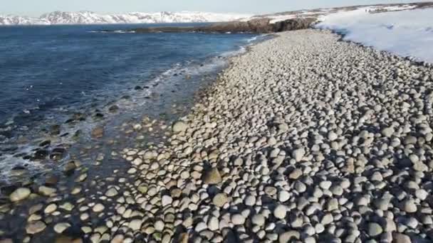 Vuelo aéreo de invierno sobre las olas rodando en la orilla ártica del océano con piedras redondas, olas oceánicas en la tormenta, video de drones de alta calidad 4k en invierno — Vídeos de Stock